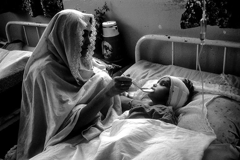 Eine Frau sitzt bei einem am Kopf verletzten Kind in einer Krankenstation.