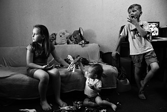 Drei Kinder in einem einfachen Zimmer schauen gespannt nach links.