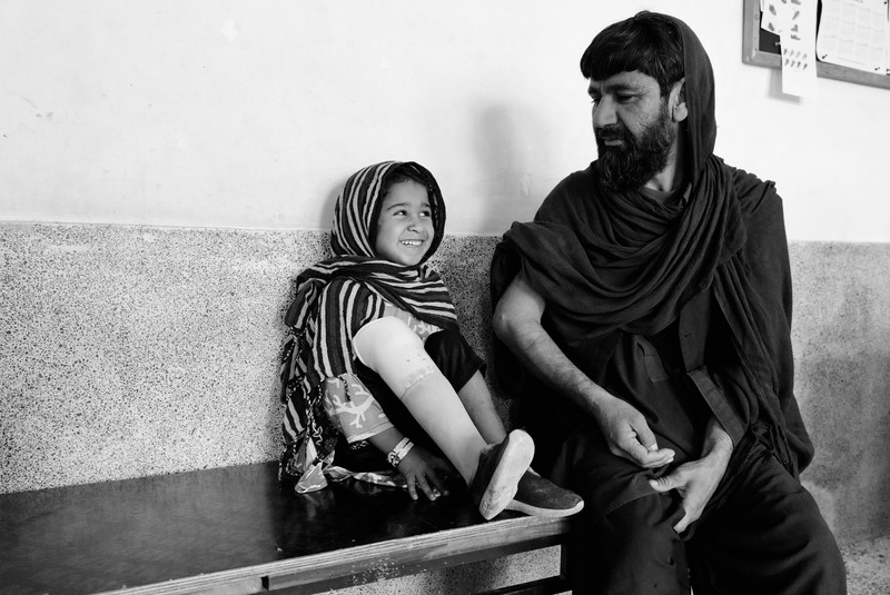 Amine und ihr Vater sitzen vor einer Wand und lächeln sich an.